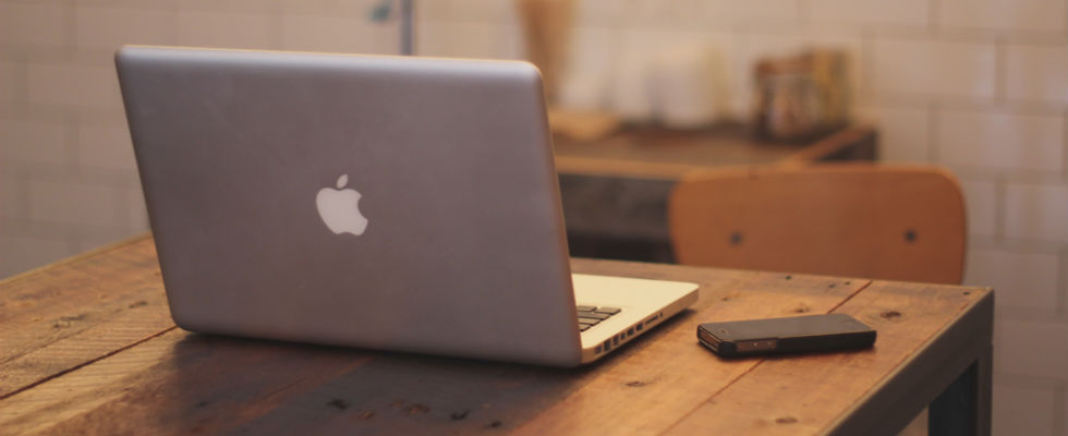An open macbook sitting on a wooden desk with the lid facing the camera